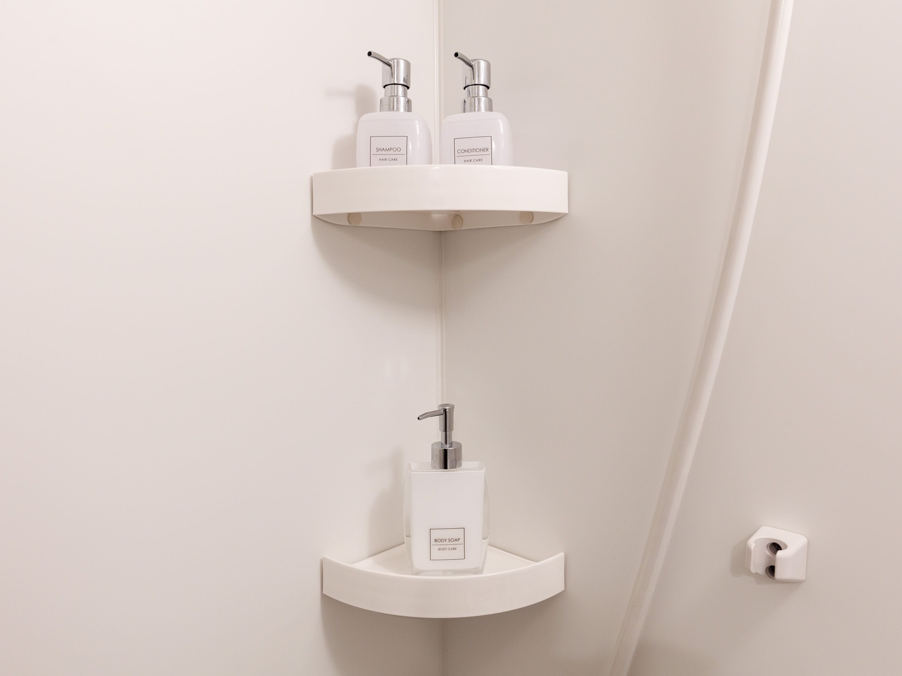 A bathroom with white shelves holding shampoo, conditioner, and body soap.