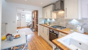 A modern kitchen with a brick fireplace, white cabinets, and a wooden countertop. - Beachcomber, Aldeburgh (Suffolk)