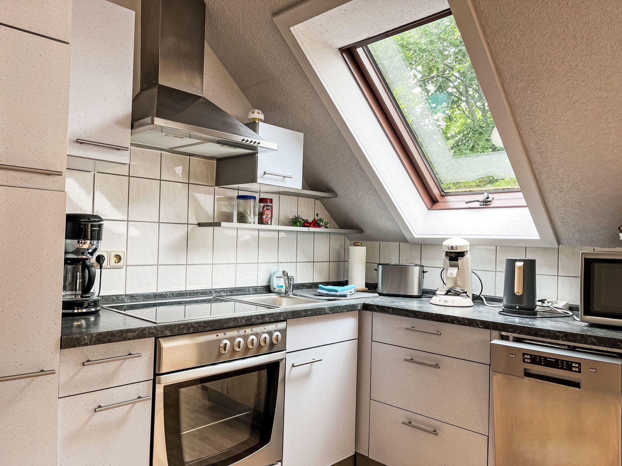A modern kitchen with a skylight, stainless steel appliances, and a view of greenery outside.