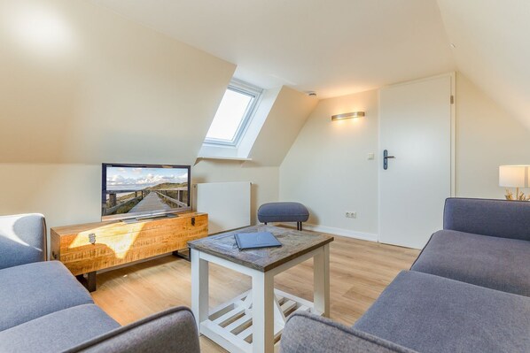 A cozy loft bedroom with a skylight, a TV, a wooden dresser, and a gray sofa.