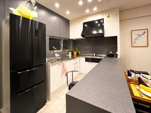 Cozinha moderna com frigorífico preto, pia de aço inoxidável e televisão de ecrã plano montada sobre a bancada.