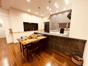 Uma cozinha moderna com armários brancos, uma mesa de jantar de madeira e um revestimento escuro.