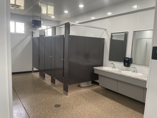 Un baño moderno con varios cubículos oscuros, un lavamanos con espejo y un secamanos.