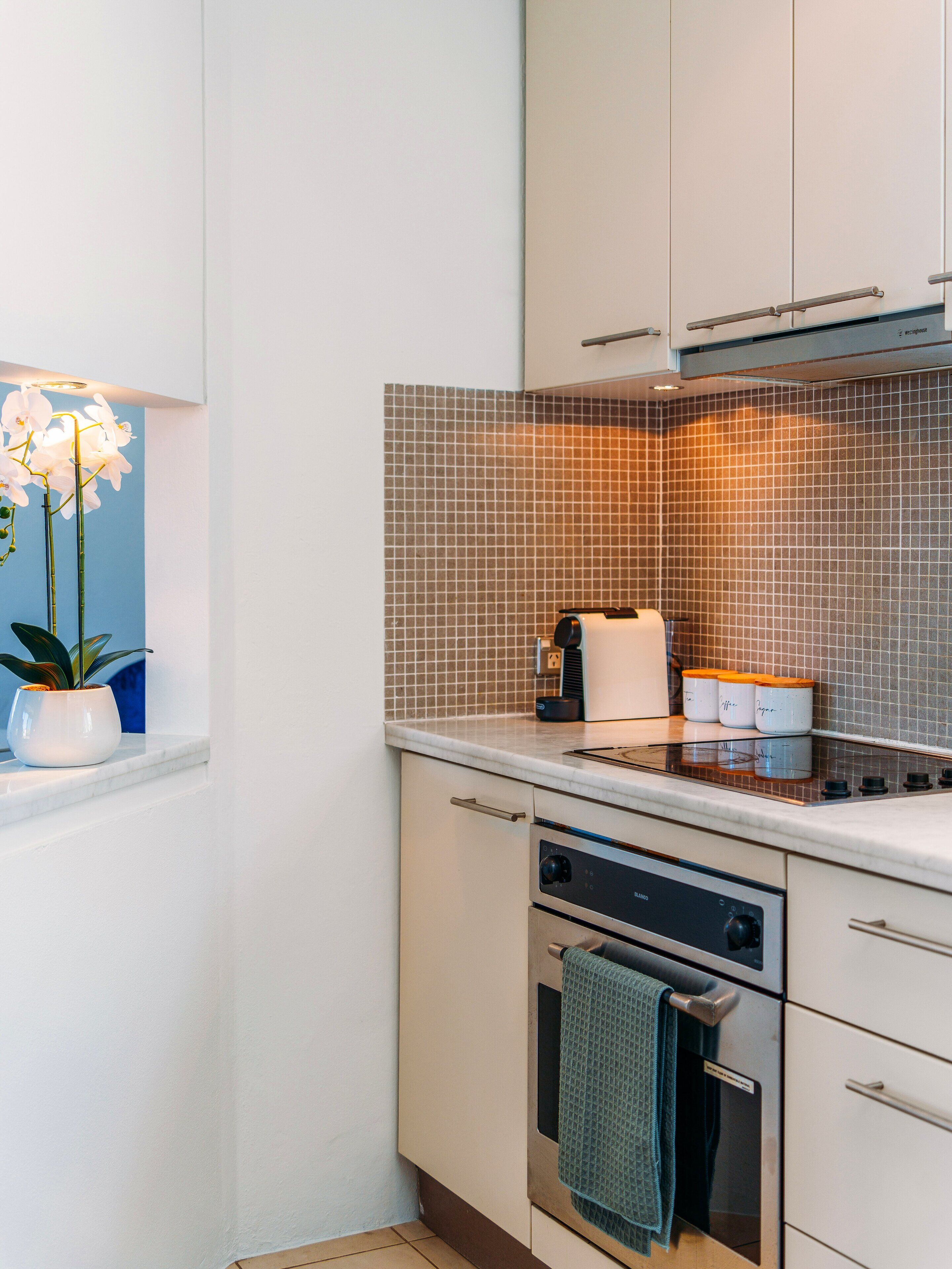 A modern kitchen with white cabinets, a tiled backsplash, a stove, and a built-in oven.