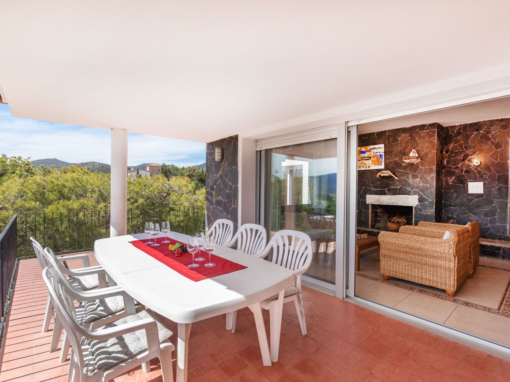 A balcony with a dining table set for four, white chairs, and a red placemat.