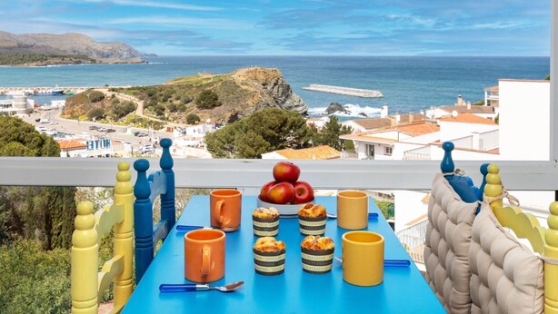 A balcony with a table set for breakfast, overlooking a coastal view with buildings and a rocky landscape. - Graciosa Blanco by Interhome (Llançà)