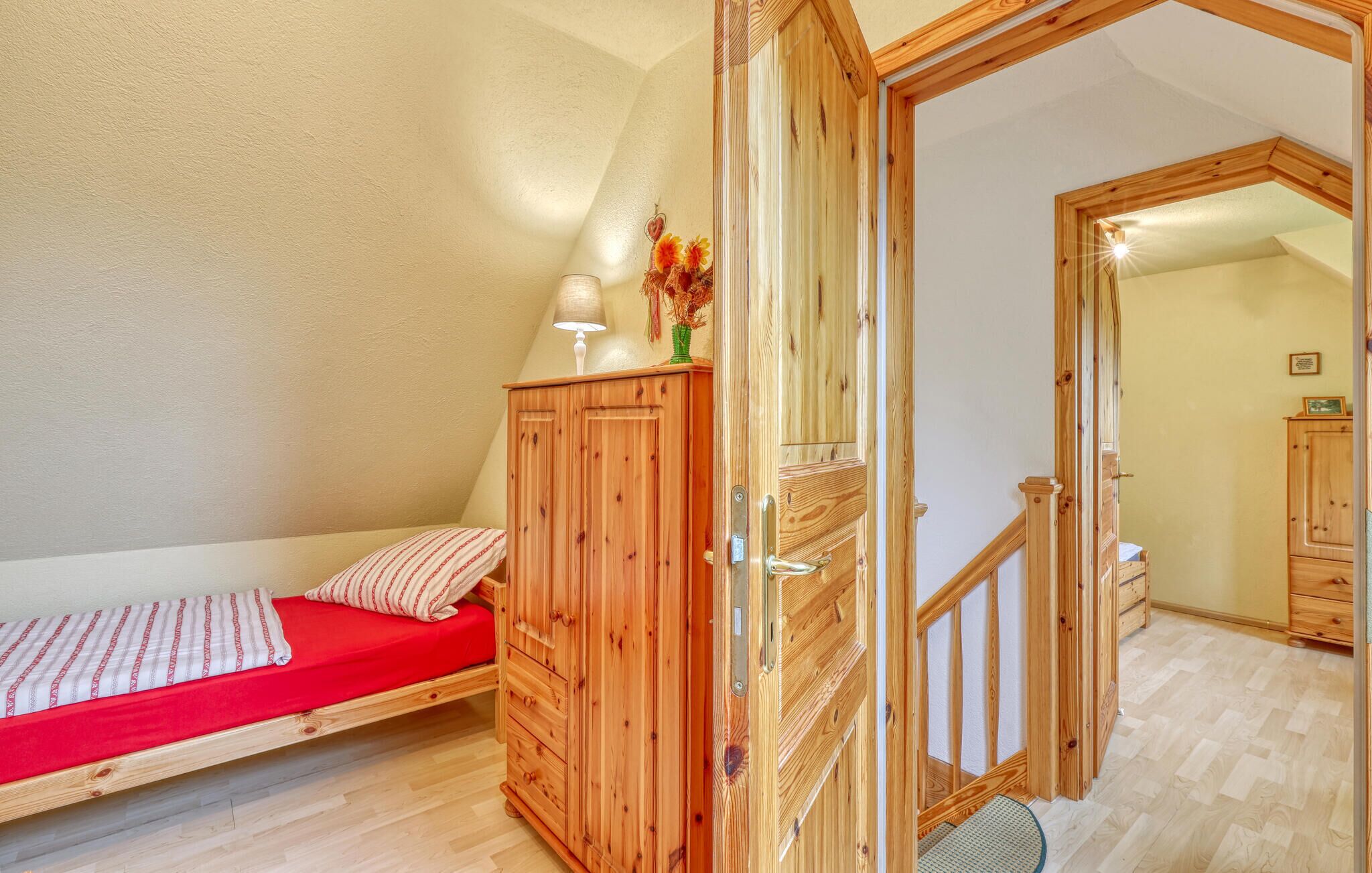 A small, cozy room with a single bed, wooden wardrobe, and a door leading to another room.