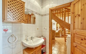 Un baño con lavamanos blanco, espejo y puerta de madera.