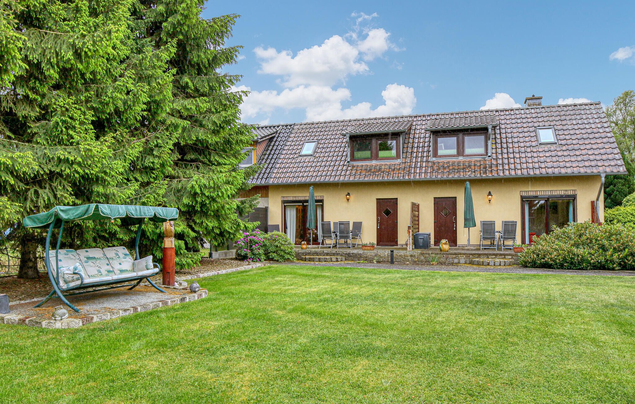 A two-story house with a tiled roof, a front porch with a swing chair, and a well-maintained lawn.