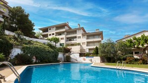 A swimming pool with a clear blue water, surrounded by a concrete deck and metal railings. In the background, there are multi-story buildings with balconies and greenery. - Mediterrani by Interhome (Llançà)