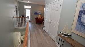 A hallway with a wooden railing, a white door, a red chair, and a small table with a model sailboat. - The Blue Pearl - Walk to the Beach in Garden City (Garden City Beach)