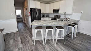 Una cocina moderna con armarios blancos, un refrigerador de acero inoxidable, un microondas y una isla grande con taburetes de bar.