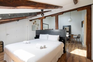 A spacious bedroom with a large bed, wooden beams, a desk, and a chair.