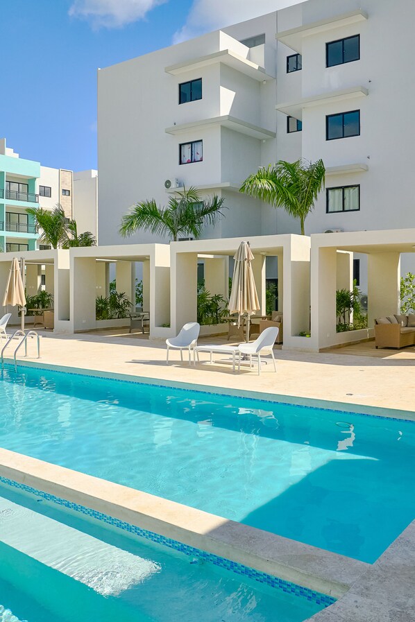 A modern hotel with a swimming pool, outdoor seating, and palm trees.