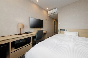 A hotel room with a bed, a desk with a chair, a television, and an air conditioning unit.