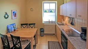 A compact kitchen with a dining table, chairs, a trash bin, a window, and basic appliances.