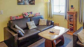 A living room with a dark leather sofa, a small wooden coffee table, and a window with curtains.