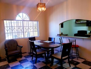 A dining area with a checkered floor, a round table, and four chairs. There is a window with bars and a chandelier above the table. - Comfy Apartments (Montego Bay)