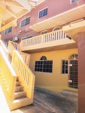 A multi-story building with a yellow staircase, balconies, and multiple windows. - Comfy Apartments (Montego Bay)