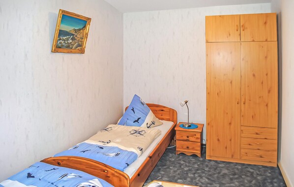 A bedroom with a single bed, a wooden wardrobe, a small bedside table, and a wall-mounted painting. - Ferienwohnung Kloster (Kloster/Insel Hiddense)