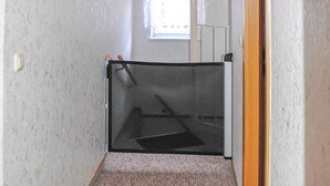 Een smalle gang met een deur die naar een kamer leidt. De gang heeft een gestructureerde witte muur en een vloerbedekking.