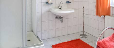 A bathroom with a white sink, a shower, and a red rug.