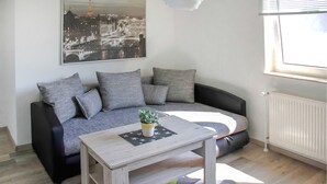 Een moderne woonkamer met een grijze bank, een houten salontafel en een stadsgezichtschilderij aan de muur.
