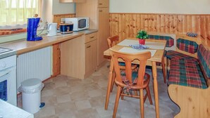 Een compacte keuken met een magnetron, broodrooster en waterkoker. Er is een eettafel met stoelen en een bank met een ruitkussen.