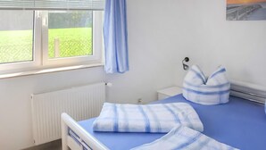 Een slaapkamer met een bed, een raam met uitzicht op groen, een radiator en een nachtkastje met een lamp.