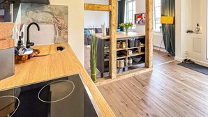A modern kitchen with a wooden countertop, black stove, and a wooden shelf unit with kitchenware. - Ferienwohnung Blankenhagen (Blankenhagen)