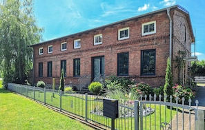 A two-story brick building with a symmetrical facade, a central entrance with a door, and a small porch area. - Ferienwohnung Blankenhagen (Blankenhagen)