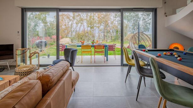 Ein modernes Wohnzimmer mit Billardtisch, einer Couch und einem Essbereich mit Stühlen.