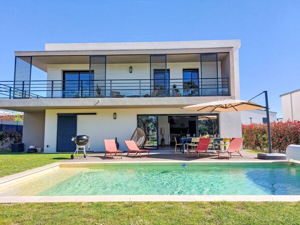 A modern two-story house with a swimming pool, outdoor seating, and a balcony.