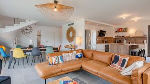 Ein modernes Wohnzimmer mit einem braunen Ledersofa, einem Couchtisch mit Früchten und einem Essbereich mit Billardtisch.