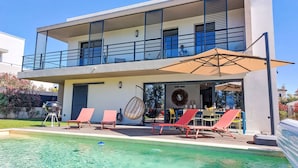 Ein modernes Haus mit zwei Obergeschossen, einem Pool, Sitzgelegenheiten im Freien und einem Essbereich.