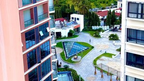A high-rise building with multiple balconies and a courtyard with a glass atrium, surrounded by greenery and other buildings.