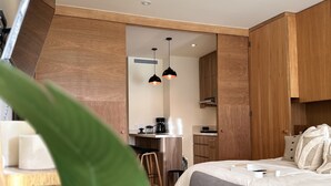 Ein modernes, kleines Schlafzimmer mit Bett, Nachttisch und einem großen Fenster.