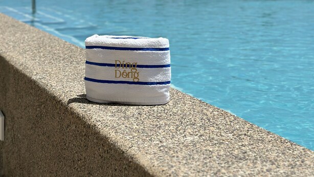 Ein Handtuch mit dem Aufdruck 'Ding Dong' am Pool.