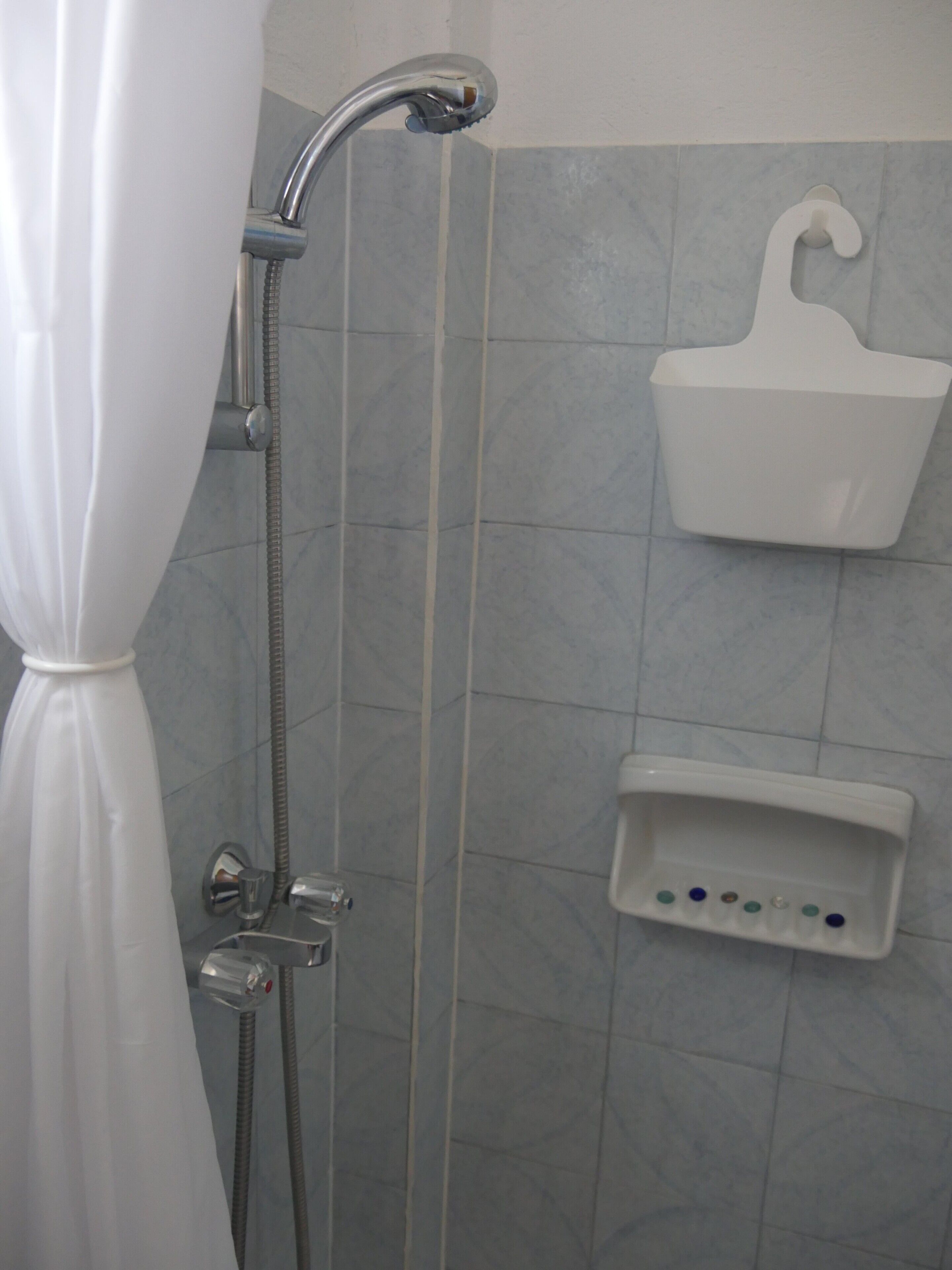 Eine Dusche mit Duschvorhang, einer Handbrause und einer Seifenschale an der Wand.