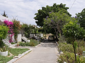 Una calle estrecha con un coche estacionado, abundante vegetación y un edificio con escaleras.