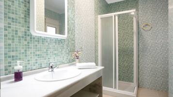 Een badkamer met een wit wastafel, een spiegel, een douche met glazen deur en een betegelde wand.