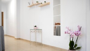 En gang med et glasbord, en pink vase med en plante, og en orkidé i potte.