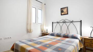 A bedroom with a bed, a nightstand, a lamp, a window with curtains, and a wall-mounted picture.