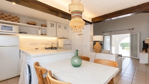 A modern kitchen with white cabinetry, a dining table with chairs, a hanging light fixture, and a view to the outside. - BINISAGOC B - Charming chalet near the sea with free WiFi (Sant Lluís)