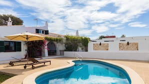 A swimming pool with a stone border, a lounge chair, and a sun umbrella. - BINISAGOC B - Charming chalet near the sea with free WiFi (Sant Lluís)