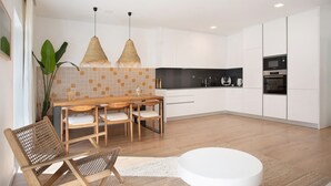A modern kitchen with white cabinets, a wooden dining table, and two hanging pendant lights. - Apartment 'Casa Aga Seaside Chic' with Balcony, Wi-Fi and Air Conditioning (Ericeira)
