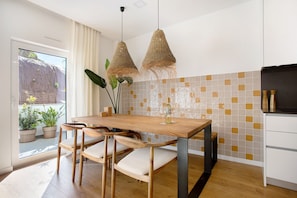 A modern kitchen with a wooden table, chairs, hanging wicker lights, and a view of the outside.