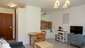 Un espace de vie compact comprenant un coin cuisine, un coin repas, un téléviseur et un petit meuble de rangement.