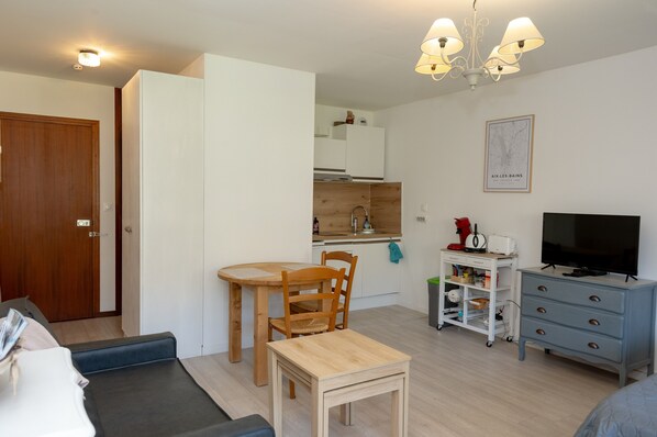 Un espace de vie compact comprenant un coin cuisine, un coin repas, un téléviseur et un petit meuble de rangement.