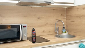 Une cuisine équipée d’un four à micro-ondes, d’un évier et d’une bouteille de produit de nettoyage.